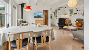 En moderne stue med spiseområde, et køkken i baggrunden og et stort vindue der lukker naturligt lys ind.