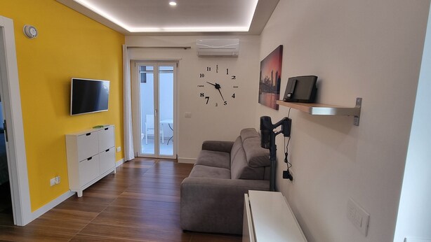 Un saló modern amb una paret d'accent groga, un televisor de pantalla plana, un sofà, una taula de centre i un rellotge.