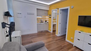 Un saló modern amb televisió, sofà, taula de centre i zona de cuina amb taulell i armaris.