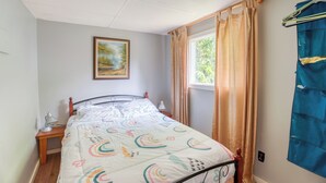A bedroom with a bed, a nightstand, a painting on the wall, and a window with curtains. - Serene Sydenham Lake Cottage - Fishing paradise (Perth Road)