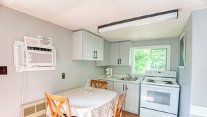 A compact kitchen with a dining table, white cabinets, a stove, and a window. - Serene Sydenham Lake Cottage - Fishing paradise (Perth Road)