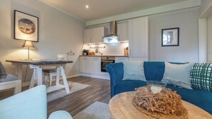 Ein modernes Wohnzimmer mit einem blauen Sofa, einem Holztisch und einem Essbereich mit einem weißen Tisch und Stühlen.