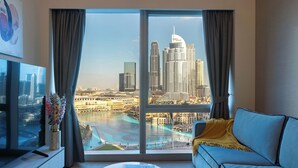 A modern living room with a large window offering a view of a city skyline, a sofa, a coffee table, and a flat-screen TV. - Full Burj Khalifa and Fountain View from All Rooms (Dubai)