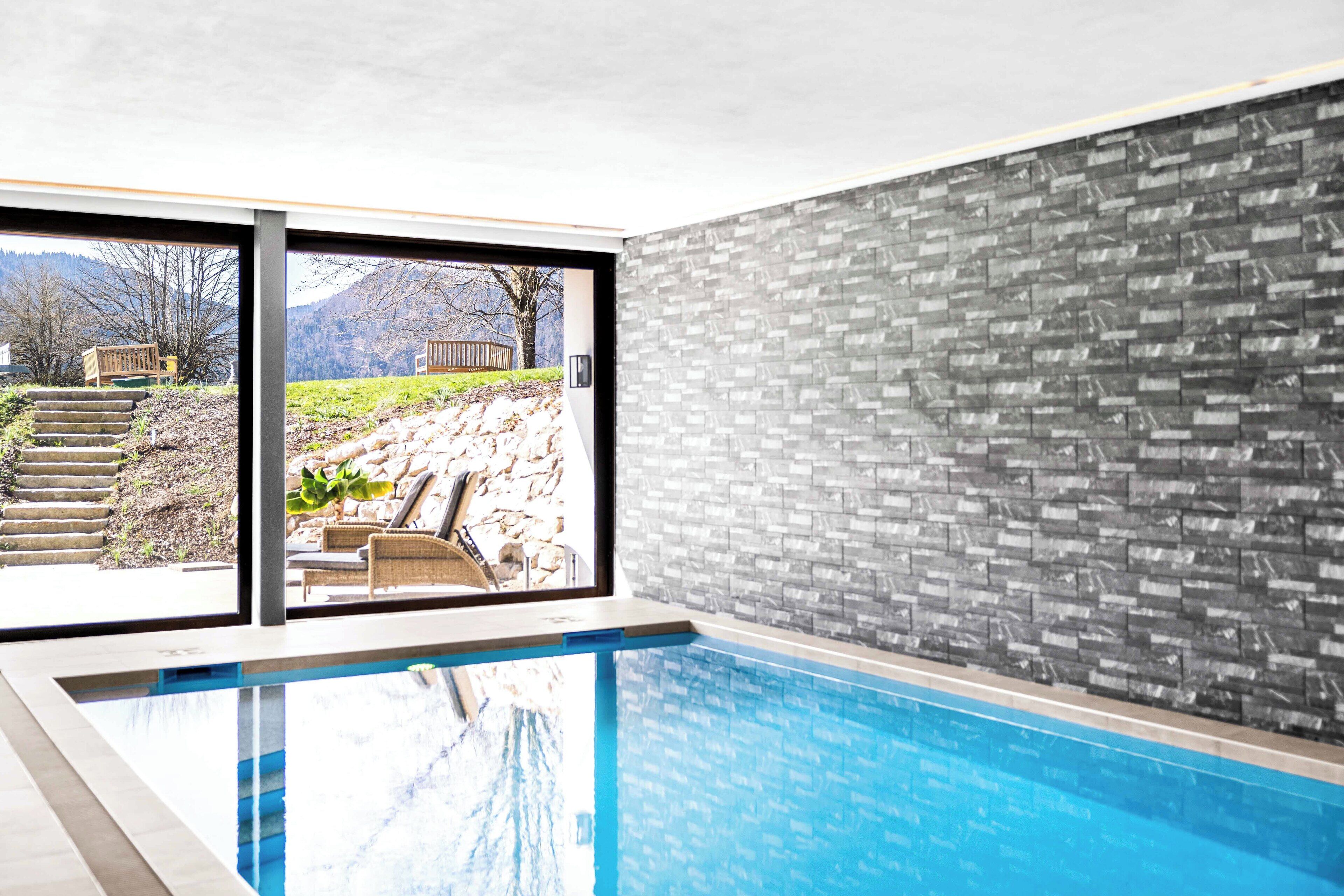 An indoor swimming pool with a view of a landscaped area outside.