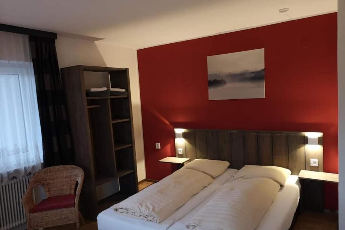 A hotel room with a bed, a wardrobe, a chair, and a painting on the wall.