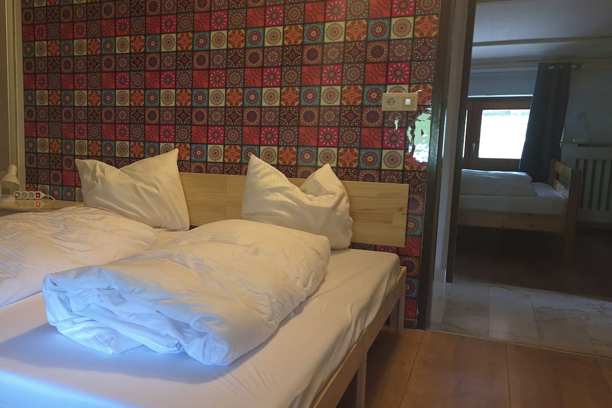 A neatly made bed with white linens, a bedside table with a lamp, and a patterned wall.