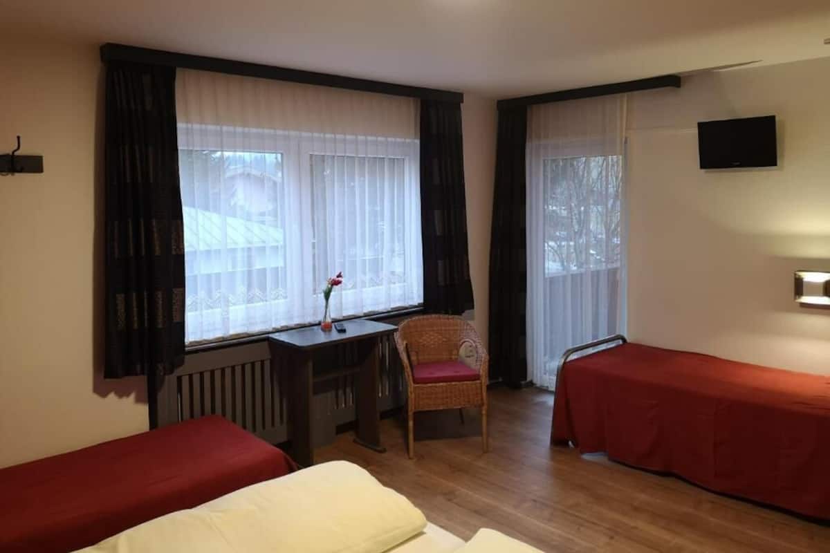 A room with two single beds, a desk with a chair, a radiator, and a TV mounted on the wall.