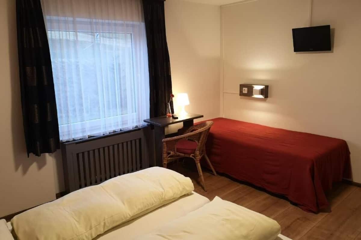 A hotel room with two beds, a desk with a chair, a TV mounted on the wall, and a window with curtains.