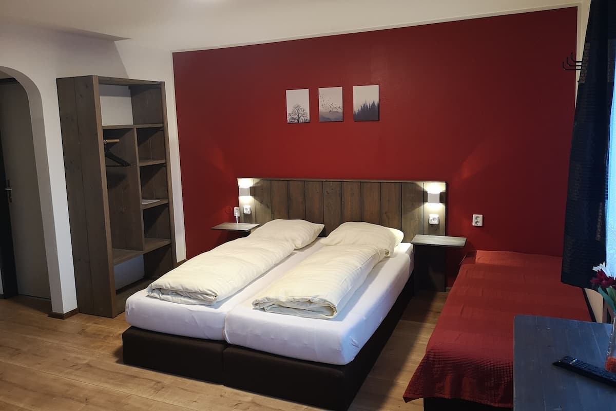 A double bed with a wooden headboard, two bedside tables with lamps, a red accent wall, and a wooden floor.