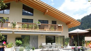Un bâtiment à deux  étages doté d’un balcon, d’un espace extérieur aménagé pour s’asseoir et de plantes en pot.
