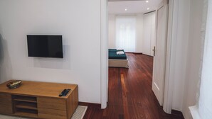 A hotel room with a wooden desk, a flat-screen TV, a bed with a green mattress, and a white door leading to another room. - Habitat 42 Roman Stay (Rome)