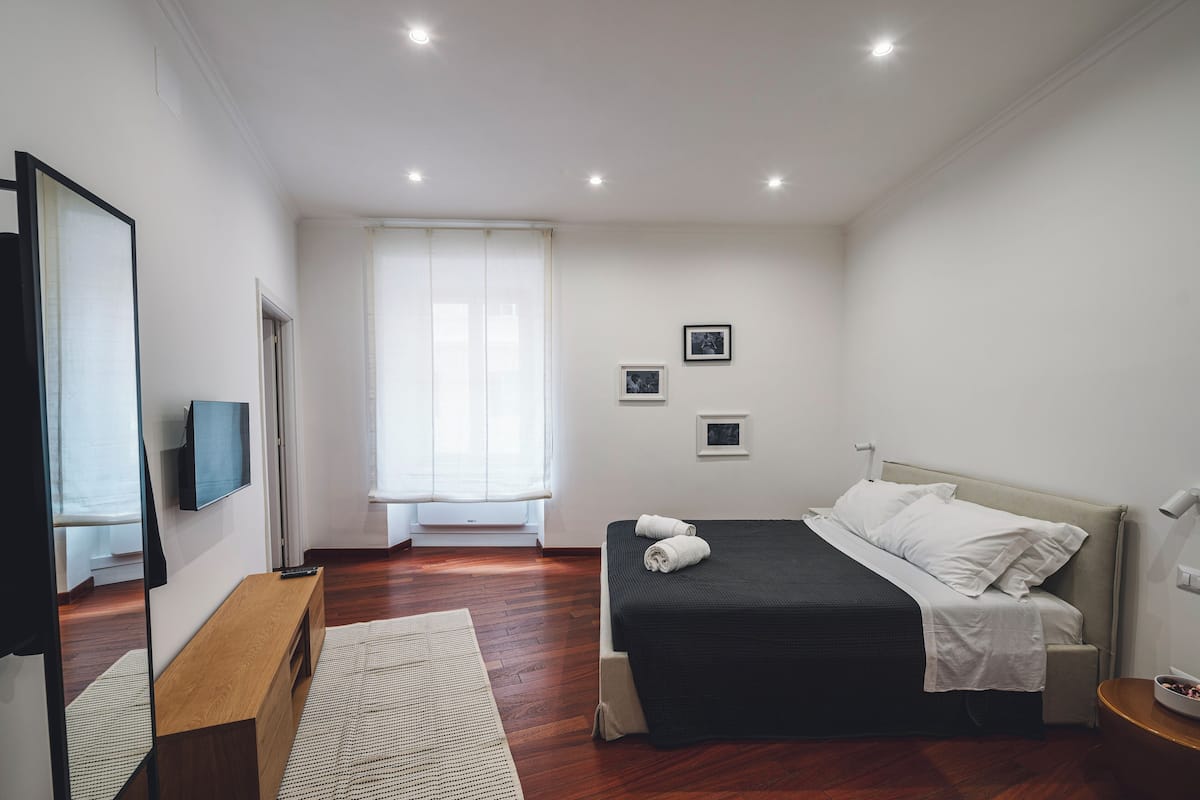 A modern bedroom with a bed, a TV, a bench, and a window with curtains.
