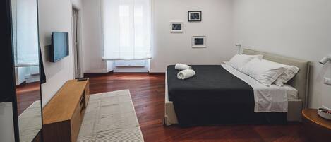 A modern bedroom with a bed, a TV, a bench, and a window with curtains.