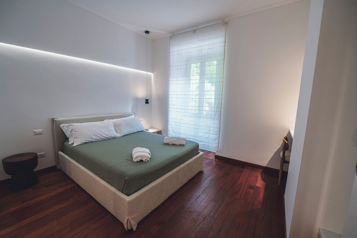 A bedroom with a bed, bedside table, and a window with blinds.
