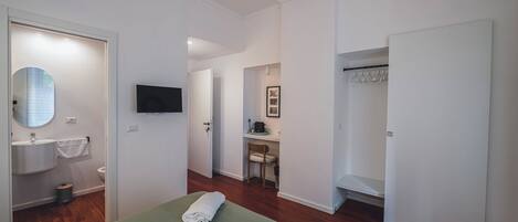 Habitación de hotel con cama, lavamanos, inodoro, silla y televisor.