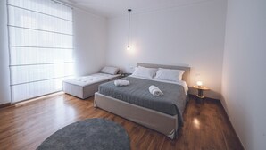 A modern bedroom with a large bed, a smaller sofa bed, a bedside table with a lamp, and a large window with blinds. - Habitat 42 Roman Stay (Rome)