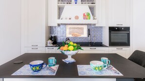 A modern kitchen with white cabinets, a blue and white backsplash, and a dining table set with blue and white patterned placemats and cups. - King Apartment - Positano Center (Positano)
