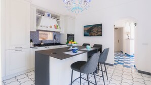 A modern kitchen with white cabinets, a central island, a chandelier, and a checkered floor. - King Apartment - Positano Center (Positano)