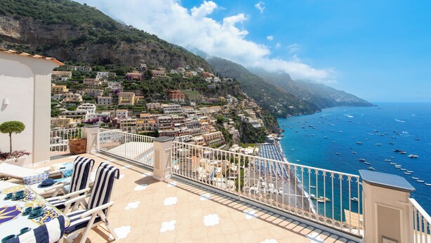 A balcony with outdoor seating and a view of a coastal town with buildings and boats. - King Apartment - Positano Center (Positano)