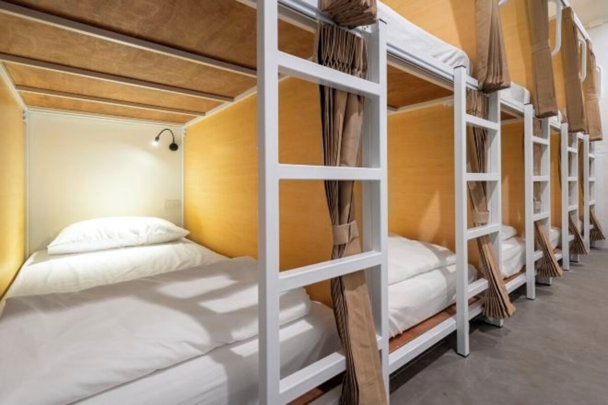 Une rangée de lits superposés aux structures blanches et aux rideaux beiges, disposés dans une chambre d’hôtel.