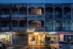 A hotel named "KUHA" with a visible entrance, a closed shop to the left, and a massage service sign to the right. - Kuha Phuket Old Town (Phuket)