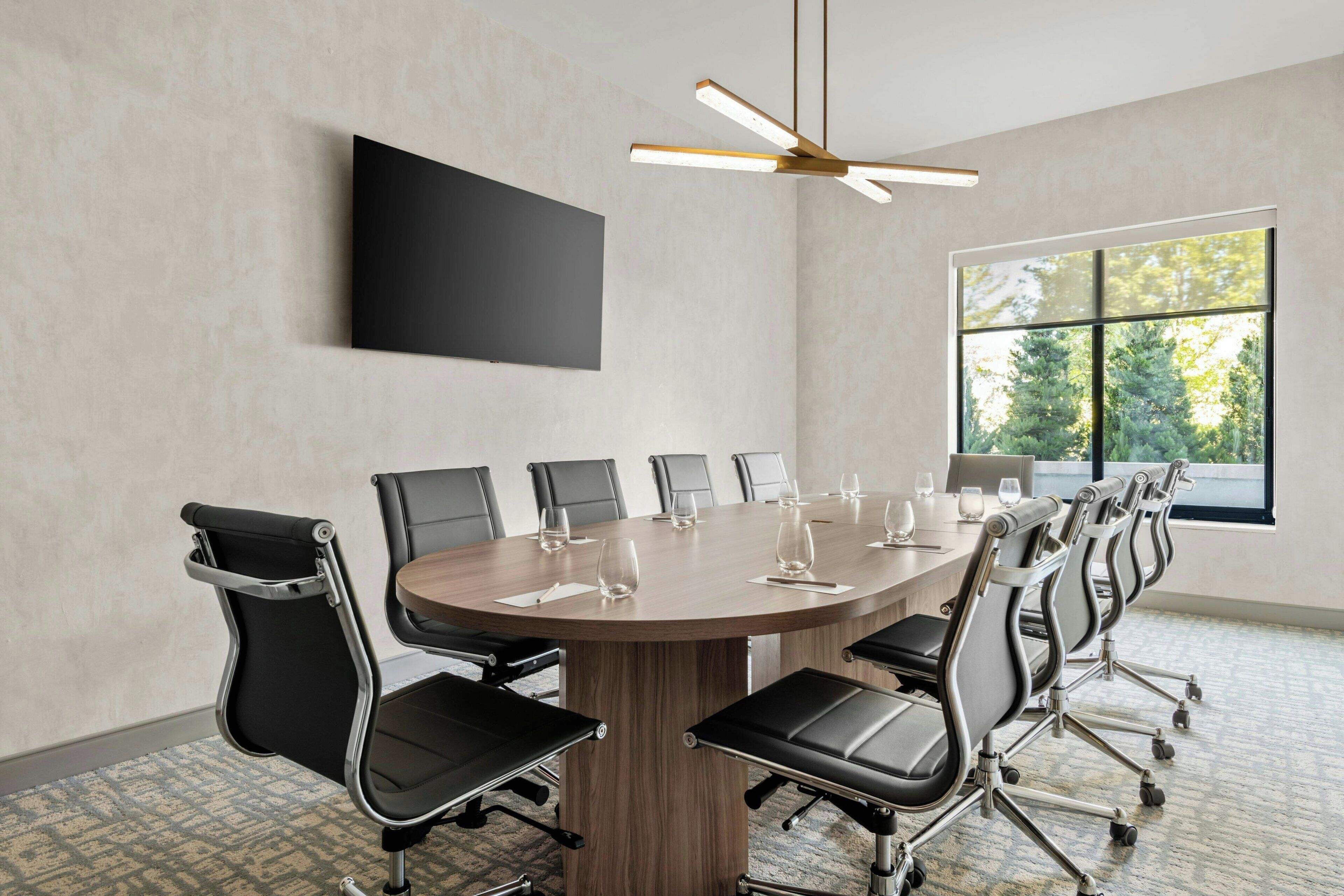 A conference room with a round table, black chairs, a flat-screen TV, and a ceiling fan.
