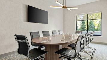 A conference room with a round table, black chairs, a flat-screen TV, and a ceiling fan.
