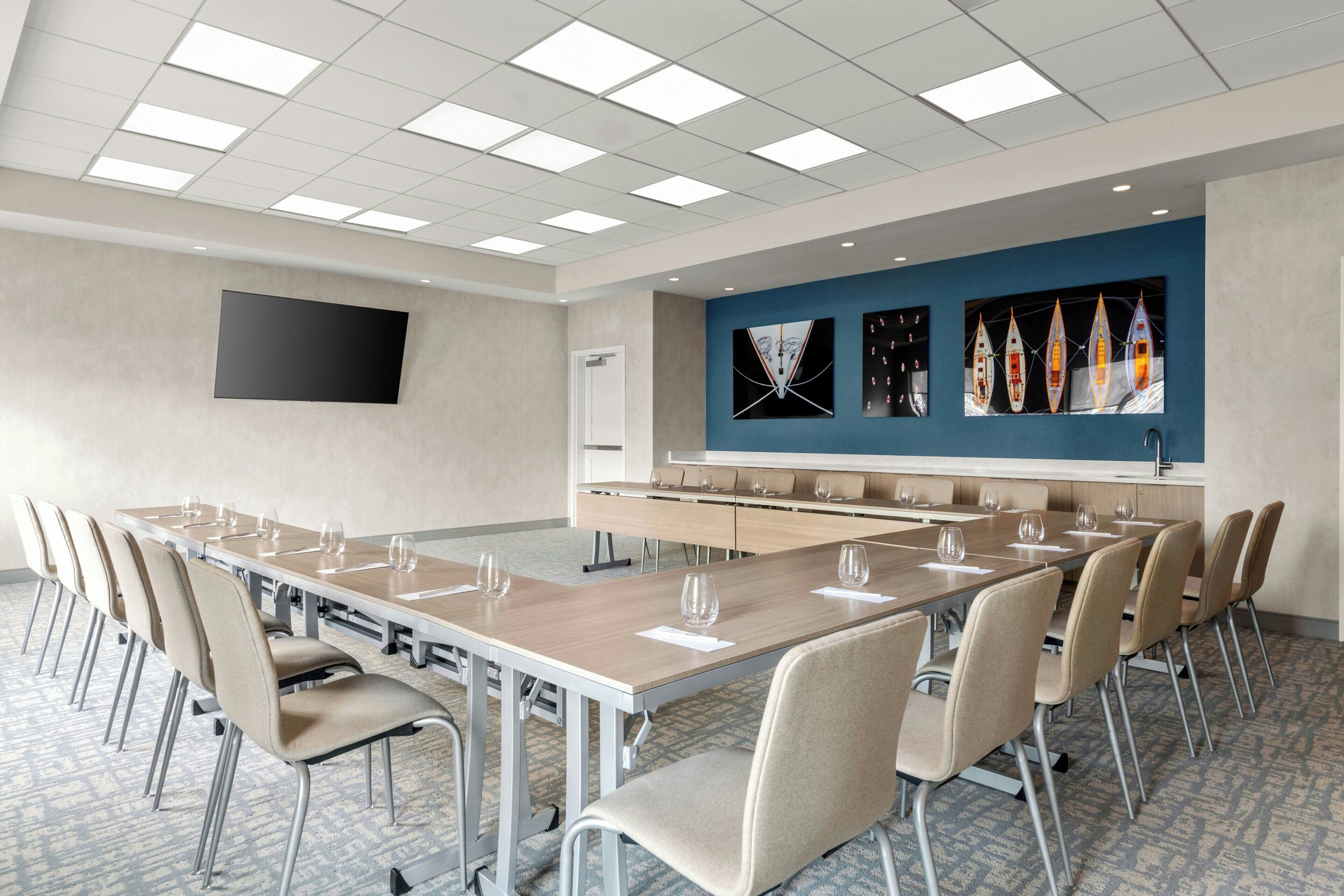 A conference room with a long table, chairs, a flat-screen TV, and artwork on the wall.