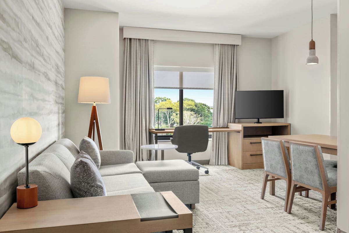 Ein modernes Hotelzimmer mit einer Sitzecke, einem Schreibtisch, einem Fernseher und Blick ins Freie.