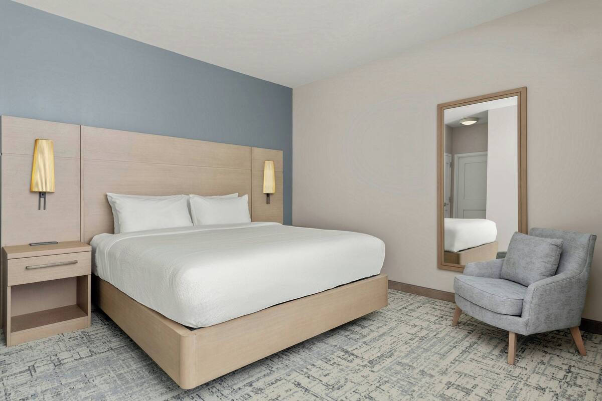 Ein Hotelzimmer mit Bett, Nachttischen, einem Sessel und einem Spiegel.