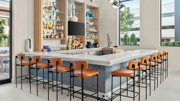 Un espace bar moderne doté d’un comptoir en marbre, de tabourets de bar et d’un grand choix de bouteilles et de verres.