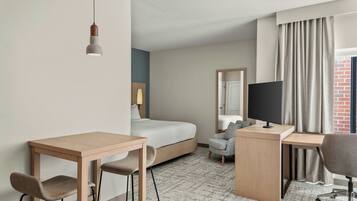 A hotel room with a bed, desk, two chairs, a TV, and a window with curtains.