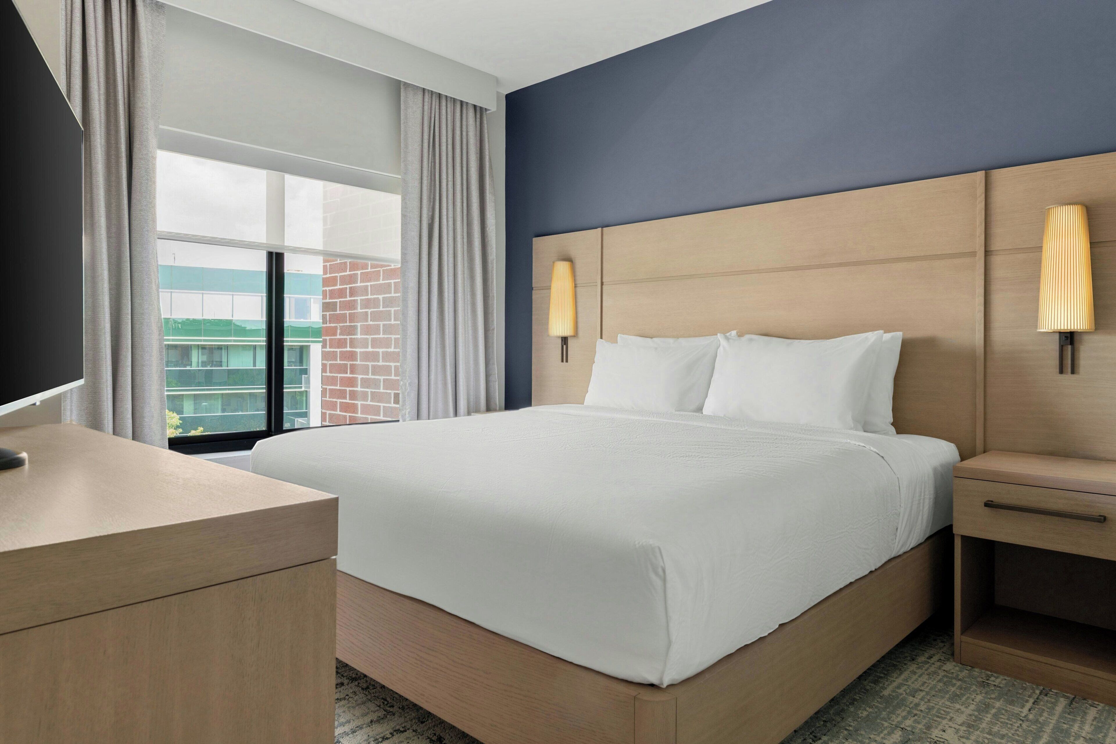 A hotel room with a large bed, a bedside table, a TV, and a window with curtains.