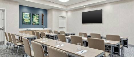 Un salón de conferencias con mesas largas, sillas, una pantalla de proyector y obras de arte en la pared.