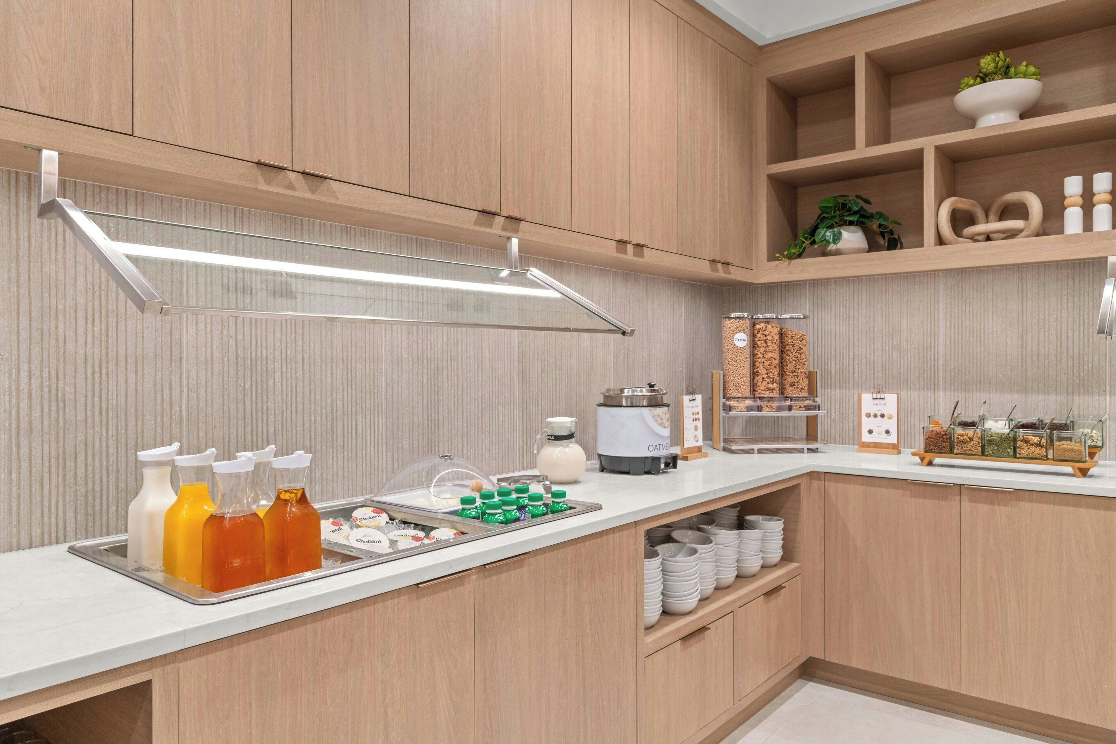 Una cocina moderna con armarios de madera, encimera blanca y diversos alimentos y electrodomésticos.