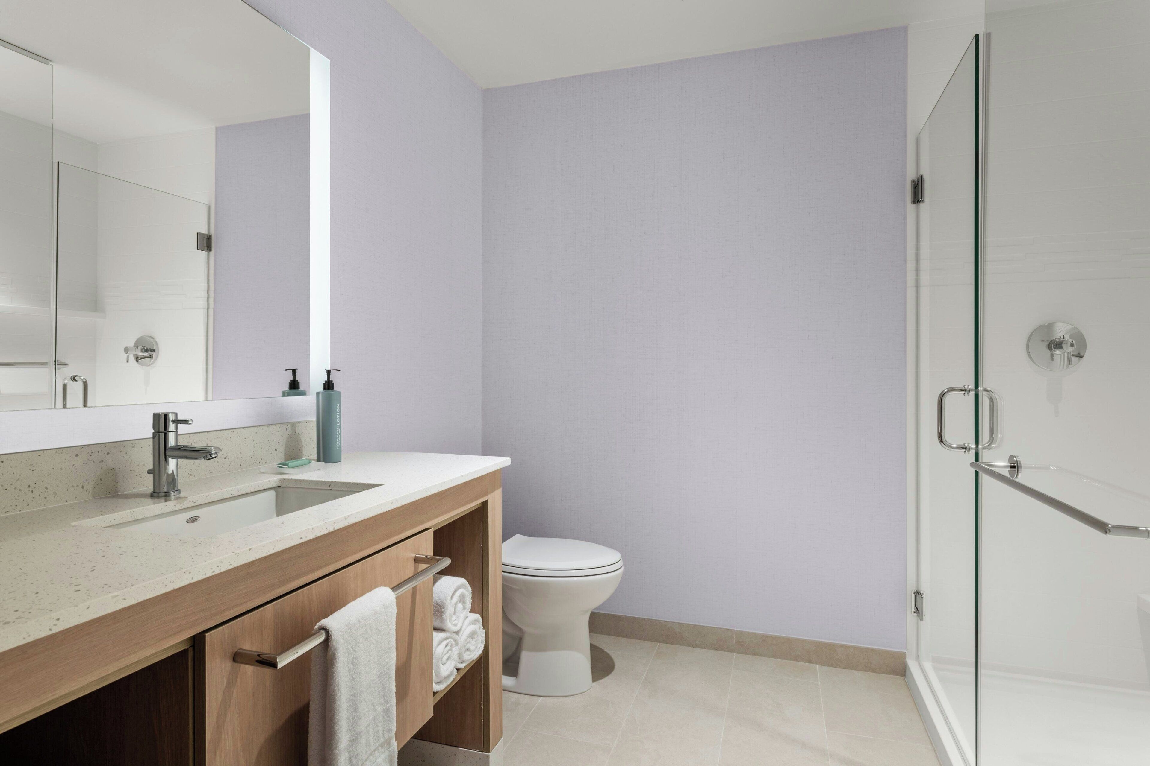 A modern bathroom with a glass shower enclosure, a white toilet, and a wooden vanity with a sink and towel rack.