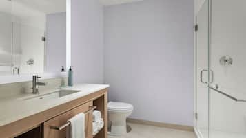 A modern bathroom with a glass shower enclosure, a white toilet, and a wooden vanity with a sink and towel rack.