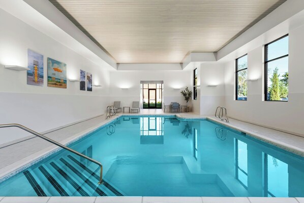 Una piscina interior moderna con agua cristalina, techo de madera y vistas a un jardín a través de un ventanal amplio.