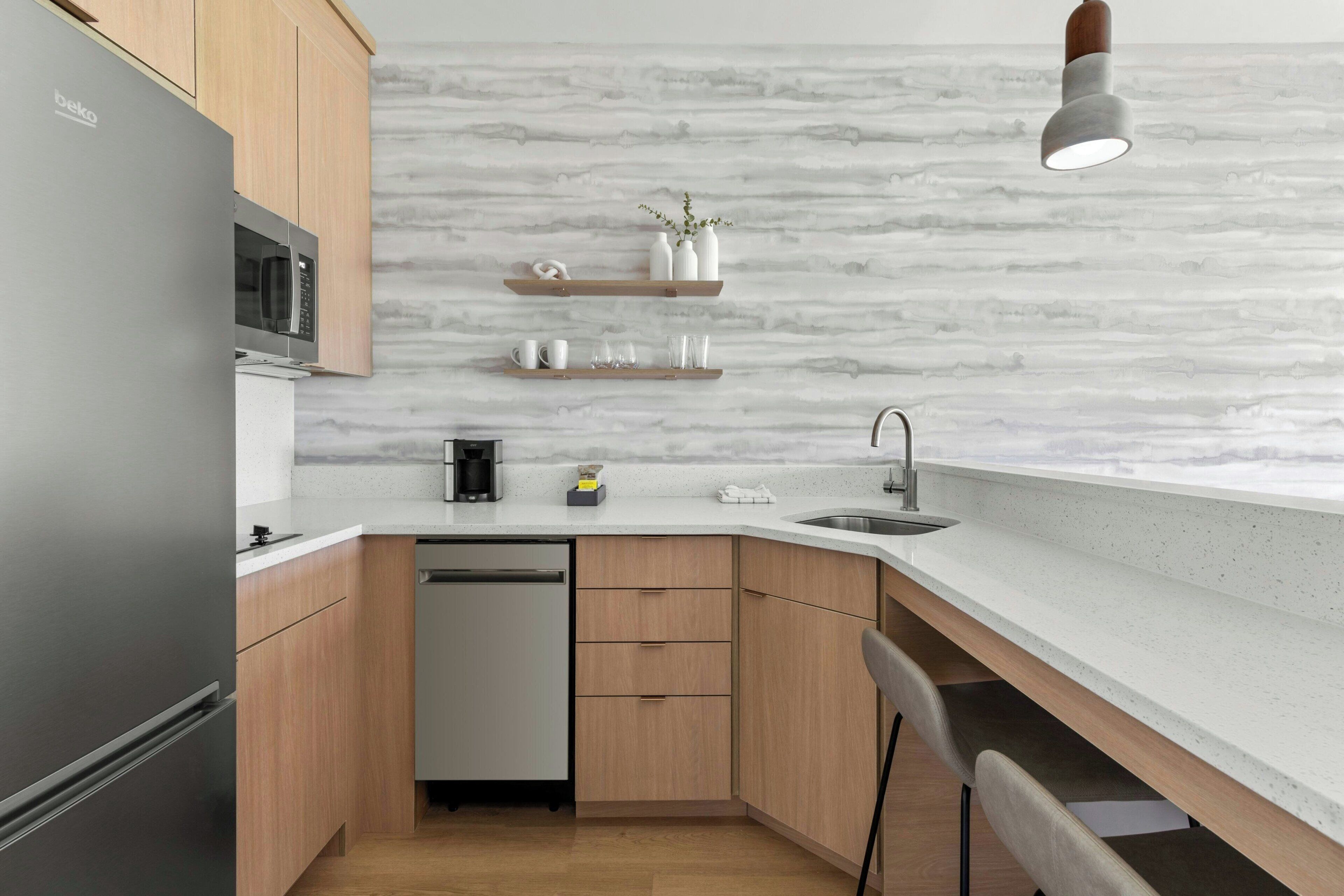 Una cocina moderna con microondas integrado, lavavajillas, armarios de madera y salpicadero de mármol.