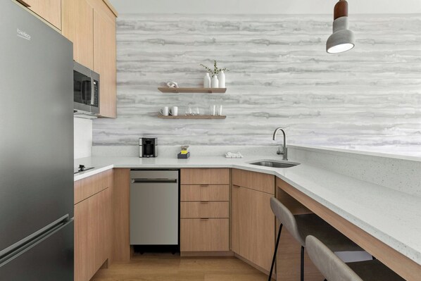 Una cocina moderna con microondas integrado, lavavajillas, armarios de madera y salpicadero de mármol.