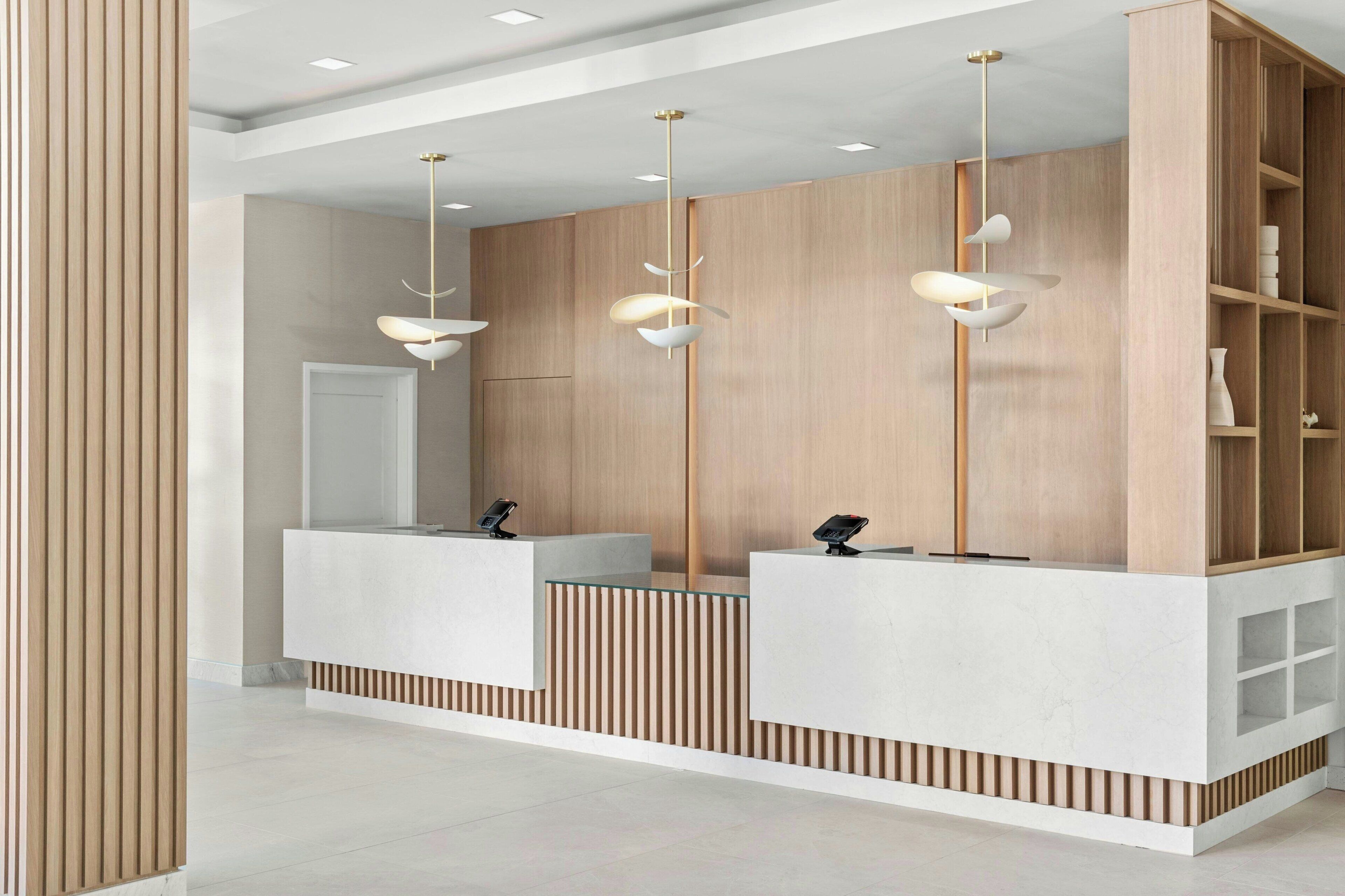 Een receptiegedeelte met een modern ontwerp, met een houten receptiebalie, een witte balie en drie hanglampen.