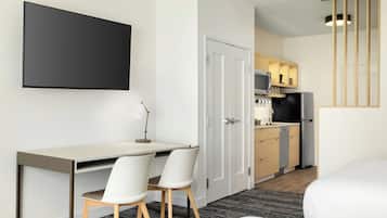 Una habitación de hotel moderna con escritorio, dos sillas, cama, televisión, zona de cocina y una escalera.