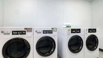Une rangée de quatre machines à laver industrielles dans une pièce propre aux murs blancs.