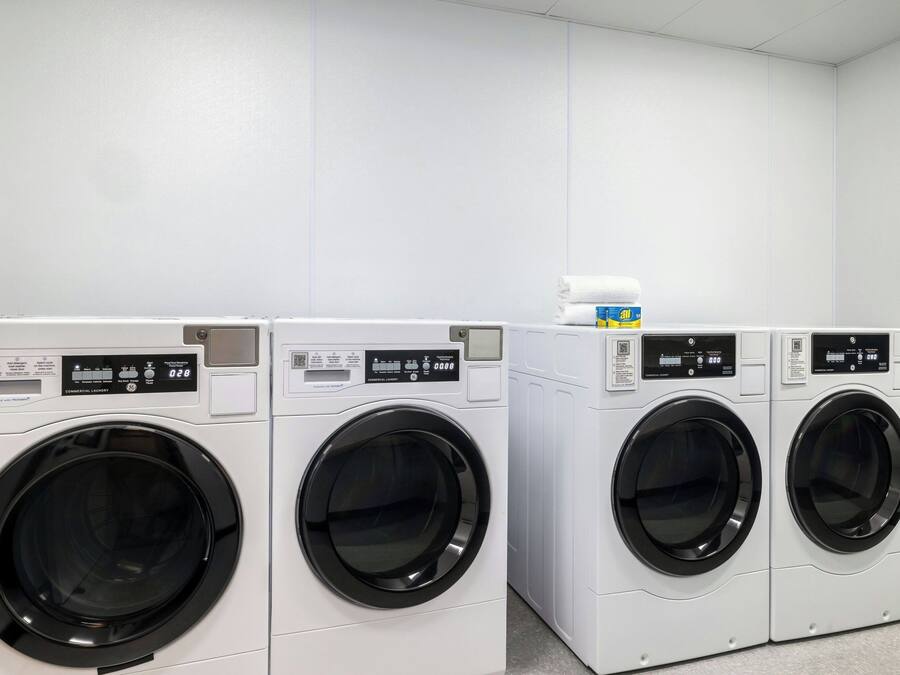 Une rangée de quatre machines à laver industrielles dans une pièce propre aux murs blancs.
