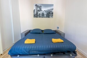 Una cama individual con una colcha azul oscuro, dos almohadas y dos toallas amarillas dobladas.