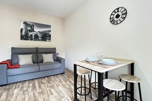 Una sala de estar moderna con un sofá gris, una mesa de comedor con taburetes y un reloj en la pared.