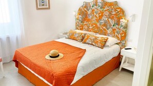 Een bed met een oranje hoofdbord en passend beddengoed, een nachtkastje met een afstandsbediening, en een ingelijst schilderij aan de muur.