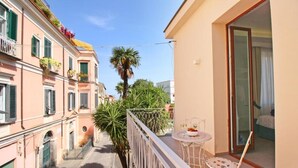 Een smalle steeg met gebouwen aan weerszijden, een balkon met een tafel en stoelen, en een palmboom.