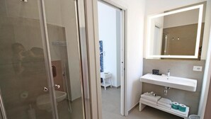 Een moderne badkamer met een douchecabine van glas, een witte wastafel met spiegel en een handdoekhouder.
