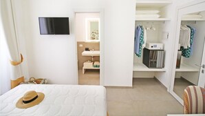 Hotelkamer met een bed, een aan de muur bevestigde televisie, een badkamer met wastafel en spiegel, en een kledingkast met hangende kleding.
